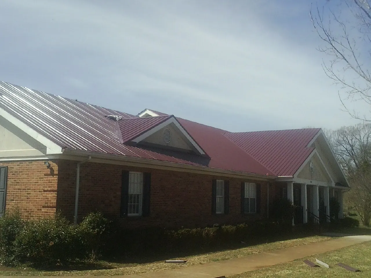 Red metal roof with gabled entries on a long brick building, from a Hail Damage Roof Repair job in Blauvelt