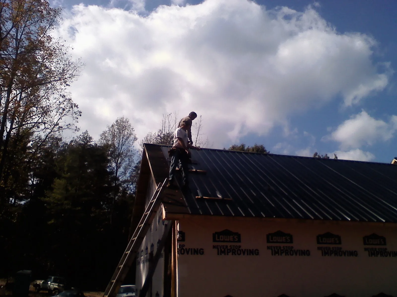 Roofer fastening dark metal panels high against a cloudy sky, from a Roof Inspection job in Blauvelt