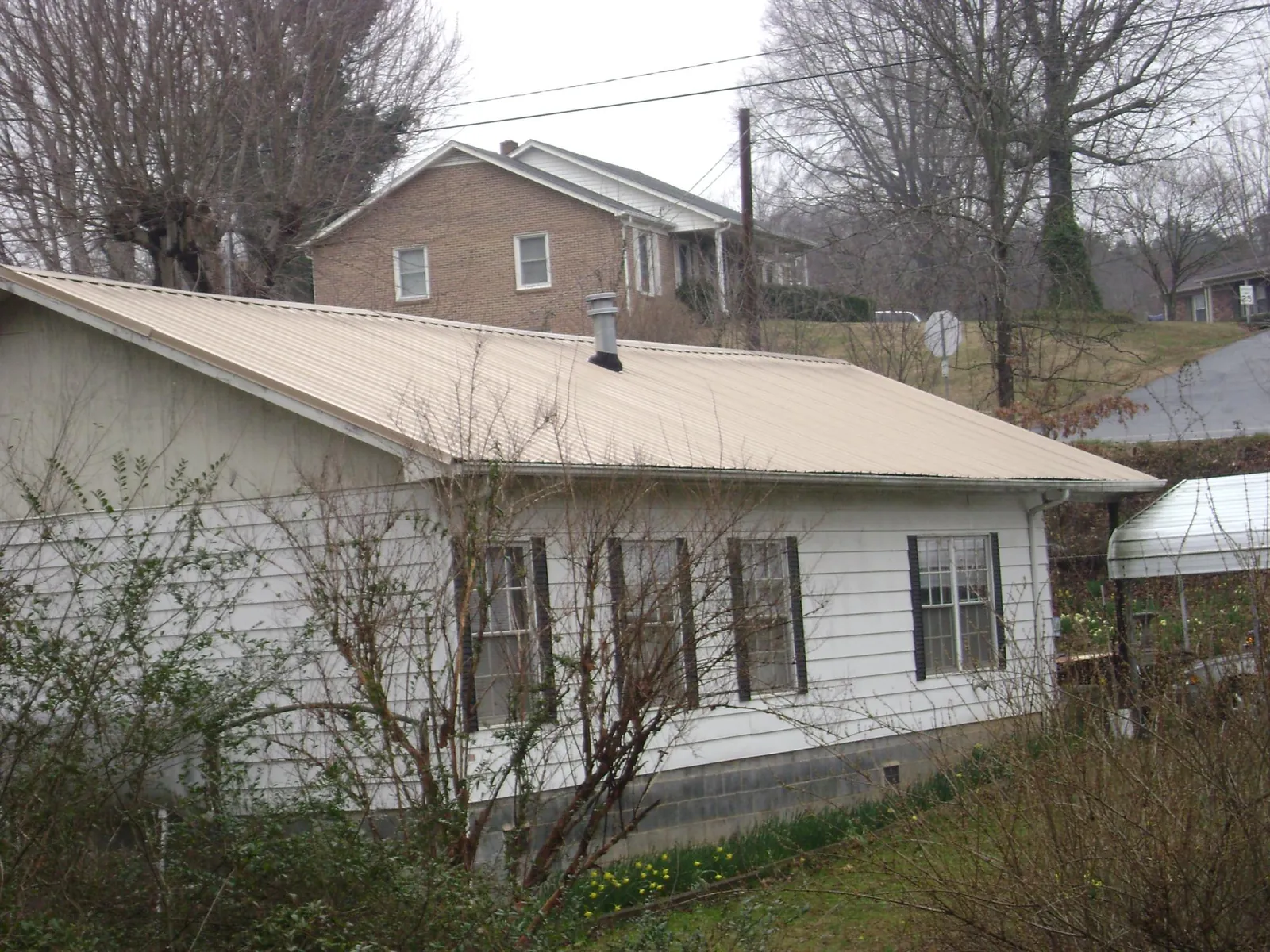 Tan metal roof on a white sided house set into a hillside — Commercial Roofing by Roofing Brothers in Blauvelt